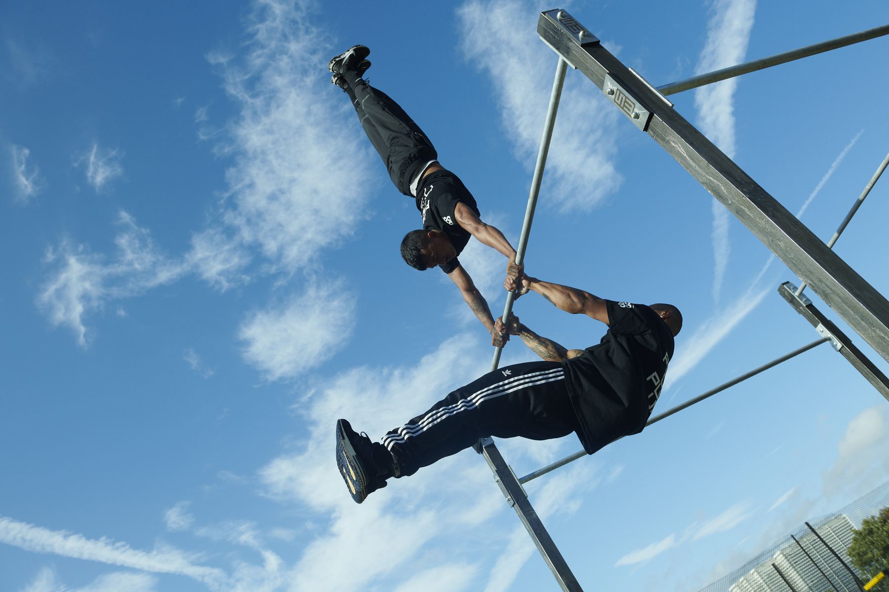 Two Steel Warriors members training on the bars against a bright sky