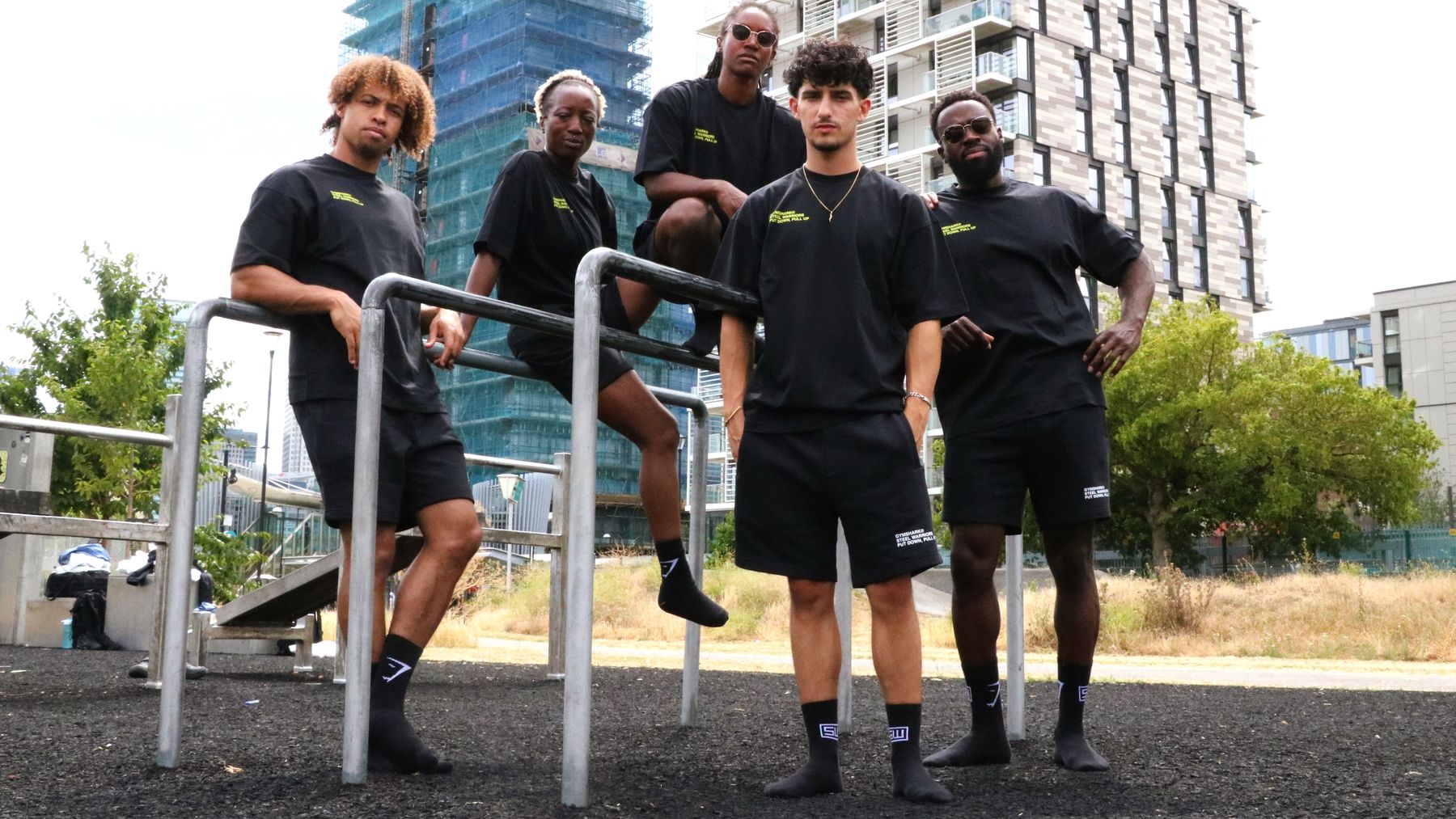 Five members of the Steel Warriors team in black Gymshark and Steel Warriors kit, posing on the bars of an outdoor gym