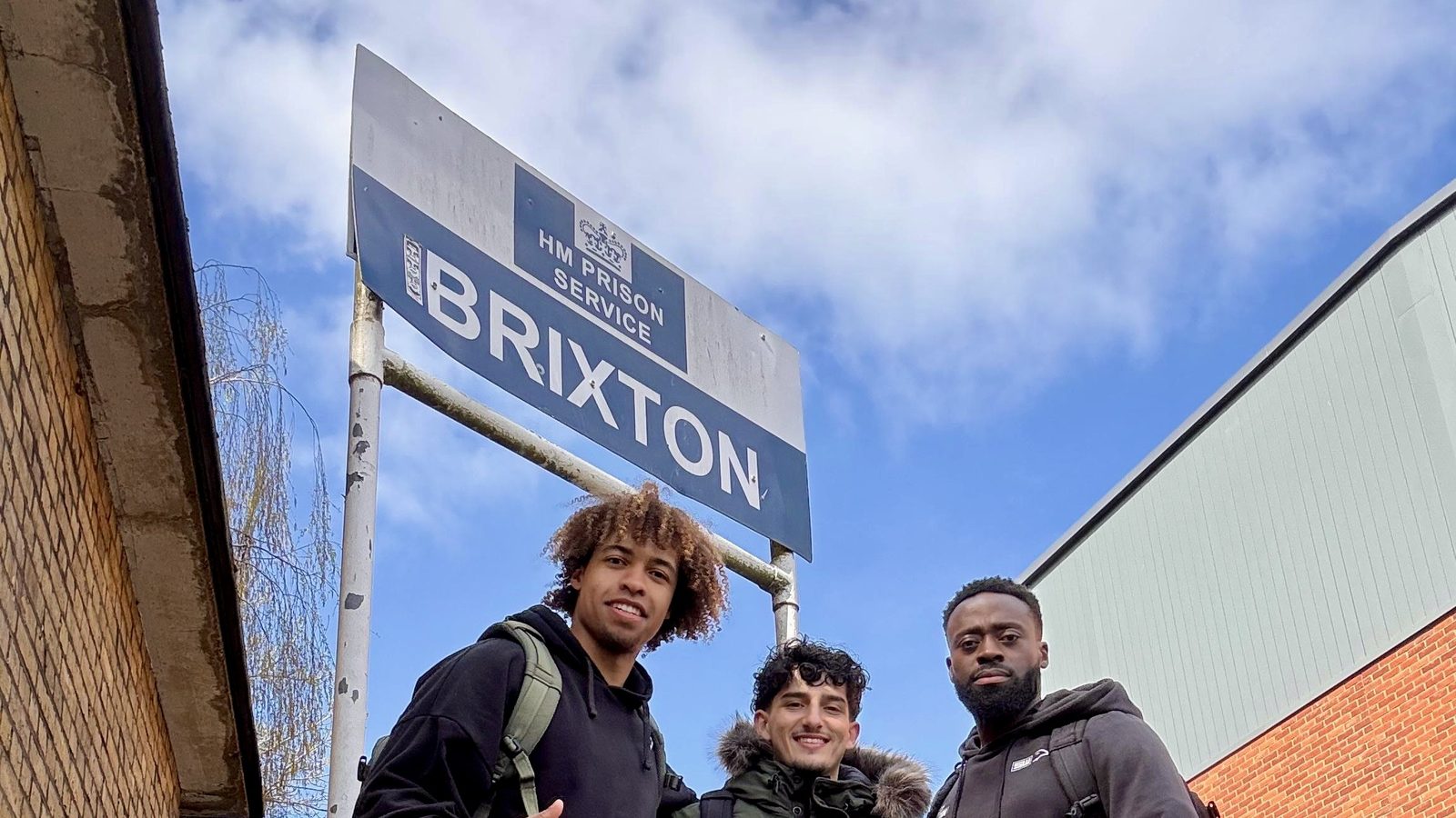 Three members of the Steel Warriors team smiling outside HMP Brixton, under the prison sign