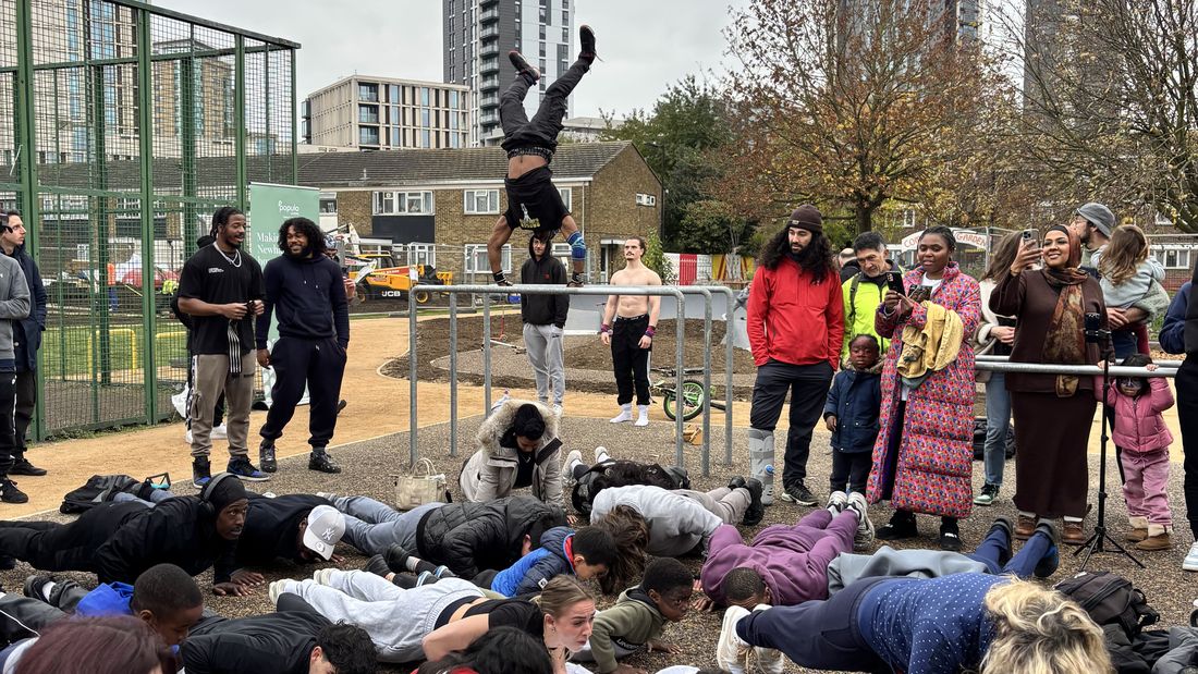 Young people doing push-ups at an event at Carpenters Estate, with someone doing a handstand on the bars behind